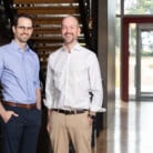 Two men standing in front of staircase smiling at camera