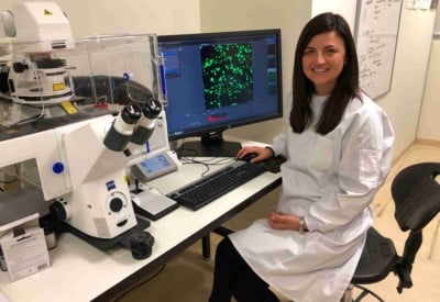 A woman wearing a white lab coat looking at microscope slides on a computer screen