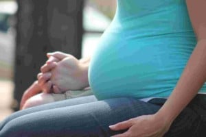Side profile of a pregnant woman in a blue t-shirt holding hands with her partner