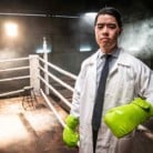 A man standing in a boxing ring wearing a white lab coat and green boxing gloves