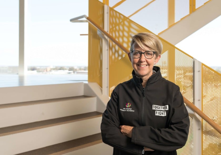 A blonde woman wearing a black jacket standing in a yellow stairwell
