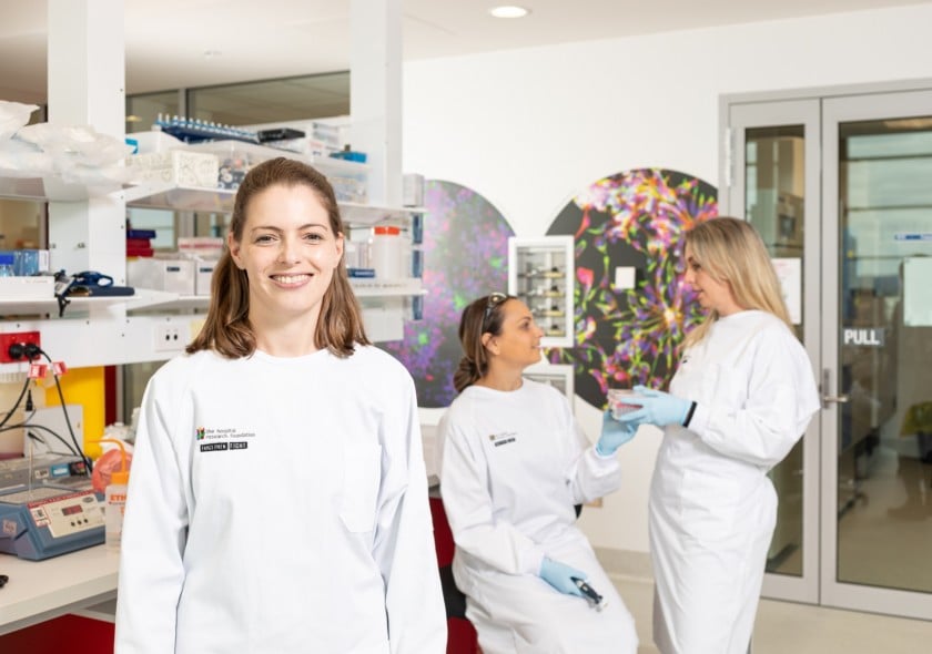 Three researchers in a lab, one is looking at the camera and two are in the background