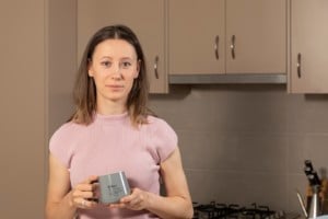 Kidney disease fighter Adela smiles at the camera. She is in her kitchen holding a mug