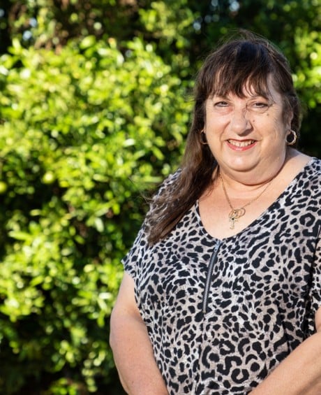Cancer fighter Beth smiles at the camera in her garden, surrounded by trees