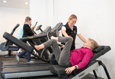 Woman instructor helping a lady on an exercise machine in a gym setting