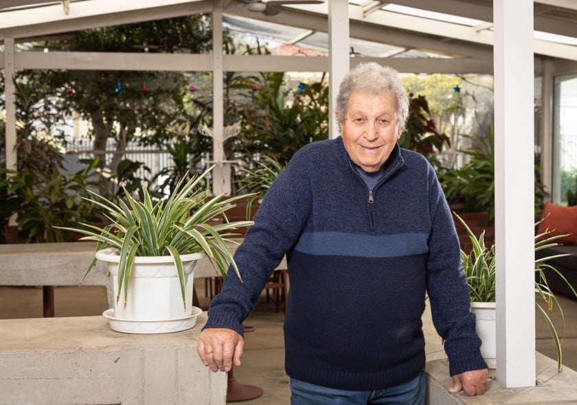 Prostate cancer fighter Con smiles at the camera on his back veranda surrounded by plants