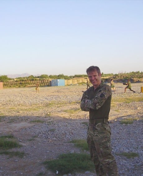 Veteran Curtis Steiger smiles at the camera. He is in uniform and a training barracks can be seen in the background.
