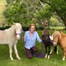 Donna from Nolton Park Horses smiles at the camera surrounded by three horses - one white, one black, and one caramel