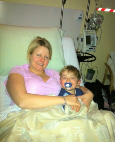 Breast cancer fighter Michelle lays in her hospital bed with her 4-year-old son. Michelle is wearing pink and her son is wearing blue