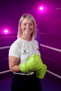 THRF Group Chief Operating Officer, Briony Marshall smiles at camera. She is wearing boxing gloves to symbolize the fight against disease.