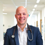 Associate Professor Johan Verjans smiling at camera in hospital corridor. His work aims to automatically convert consultations into clinical notes.