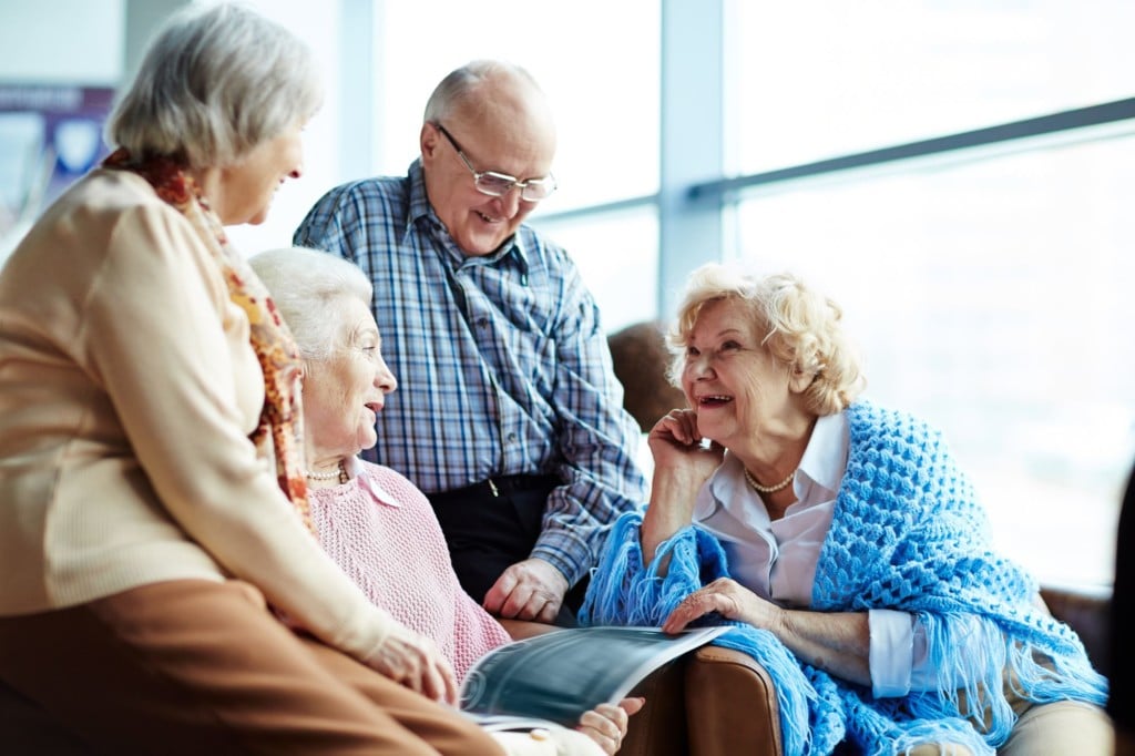 Three female and one male talk animatedly. One woman has a magazine open on her lap