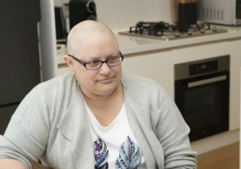 Cindy with shaved head wearing glasses sitting inside