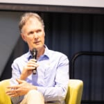Professor Paul Worley sitting with a microphone addressing an audience. He is enhancing mental health referral systems in rural areas using AI.