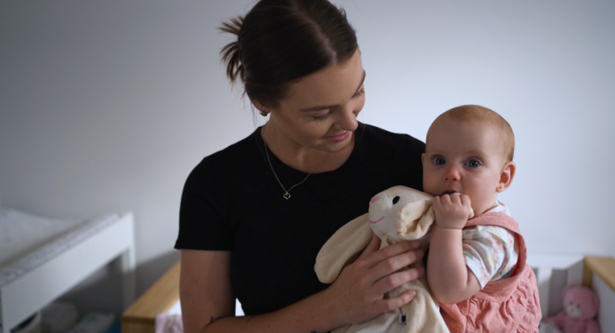 Patient Chelsea is holding baby girl in a pink dress.