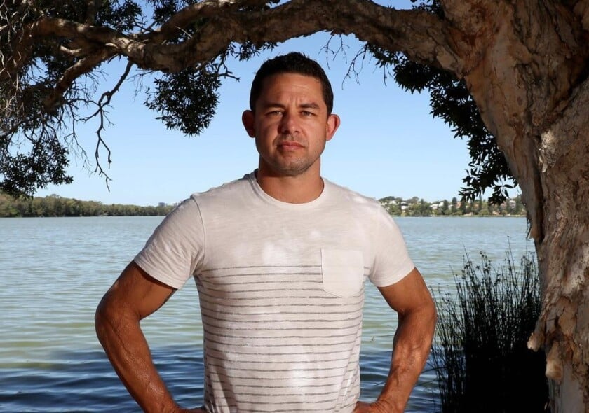 Phil Britten stands with hands on hips. Phil is wearing a white T-shirt. Behind Phil is a body of water.